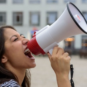 Woman yelling into a bullhorn on an urban street voicing her displaeasure during a protest or demonstration close up side view of her face